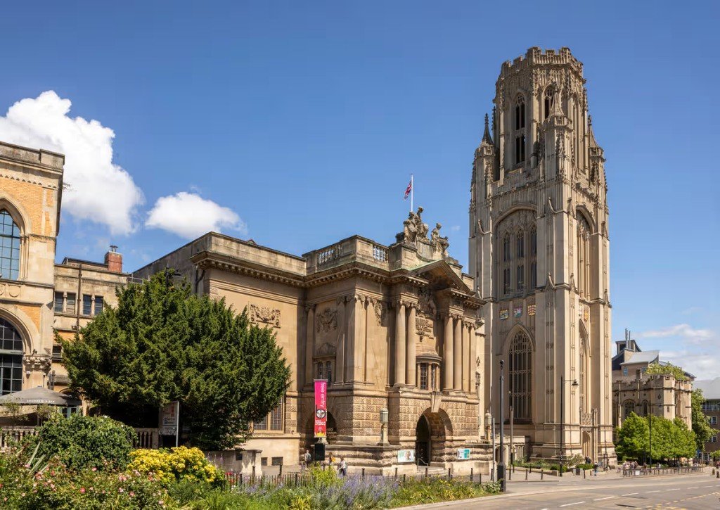 The Wills Memorial Building at the University of Bristol, a Gothic Revival stone tower beside an ornate facade under a blue sky.
